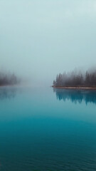 Mist hovering above still forest lake, soft aqua color palette and light cloud cover.