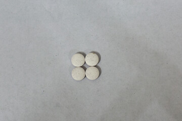 Off-white, speckled round pills arranged in a square on a light gray background. Medicine concept.