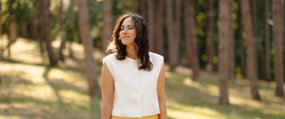 A tranquil woman is enjoying the beauty of nature, surrounded by tall trees, radiating both peace and confidence