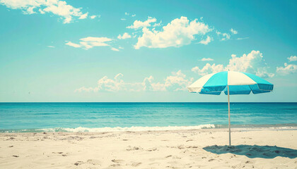 Fototapeta premium A blue and white umbrella stands alone on a sandy beach, evoking a nostalgic vintage summer vibe under clear skies. 