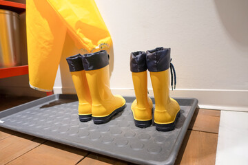 Bright yellow rubber boots on a mat beside a raincoat in a cozy indoor setting with warm tones