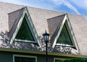 Sharp-angled A-frame dormer windows on a shingled rooftop with a lamp post in Brighton, Massachusetts, USA