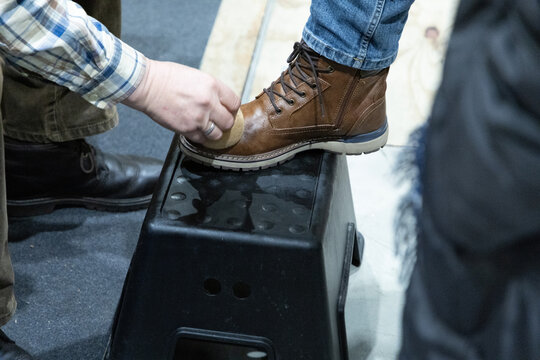 Person polishing brown leather boot while standing on a black stool in a casual indoor setting - Powered by Adobe