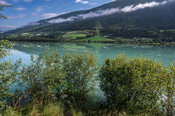 Norwegian summer, countryside reflected on the emerald green river surface, low-hanging clouds, Vågå, summer in Norway