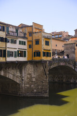 Obraz premium Colorful historic buildings with green shutters perched on Ponte Vecchio bridge over the Arno River in Florence, Italy, on a sunny summer day 