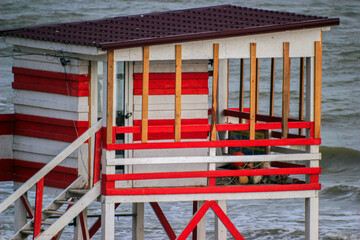 Red and white wooden lifeguard post on the shore of a stormy sea