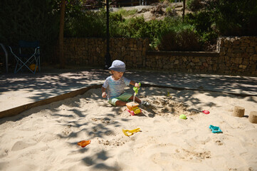 Child Playing in Sandbox with Toy Tools in Sunny Playground