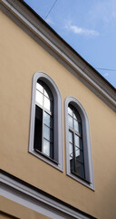 Two tall arched windows with white trim reflect the sky on the facade of a yellow classical style building