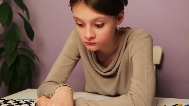 Сute tired yawning kid girl doing home exercises sitting at the table with book, copy books, pens, pencil case with surprising big eyes. Back to school. Concept education video