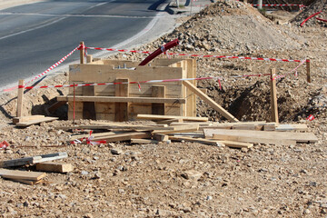 An active roadside excavation shows wooden formwork for concrete, exposed red utility conduits,...