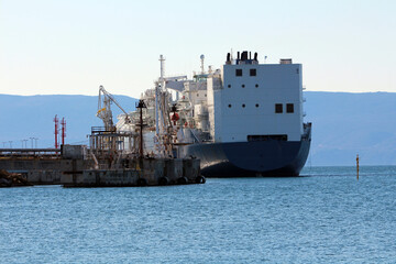 A massive oil tanker approaches a specialized loading dock equipped with pipelines and machinery...