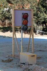 A mobile, battery-powered traffic signal with a wooden frame stands on gravel at a road...
