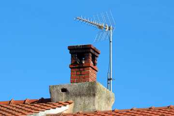 A classic red brick chimney rises above terracotta roof tiles, topped with a modern digital TV...