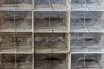 A tightly packed stack of metal lobster or crab pots showcases repeating wire mesh patterns and distinctive circular entrances, highlighting essential fishing equipment at the dock