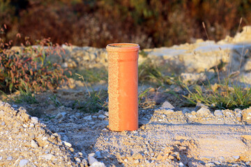 An upright orange plastic utility pipe emerges from rough gravel, partially coated with dust, highlighting new underground infrastructure installation at a construction area