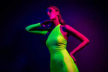 Stylish young woman in green dress illuminated by vibrant neon lighting, showcasing modern fashion
