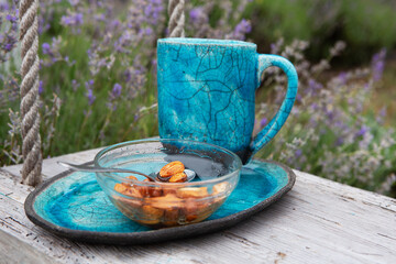 Organic gourmet breakfast. Beautiful cup of aromatic tea or coffee and a glass bowl with a mixed nuts in honey stand on a trayin a lavender field. Handmade clay products. Wooden background.	
