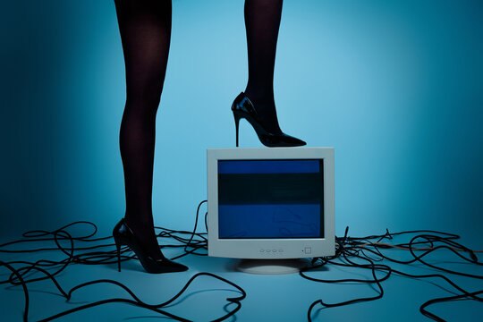 Elegant young woman in black high heels posing atop an old computer against a modern gradient studio background