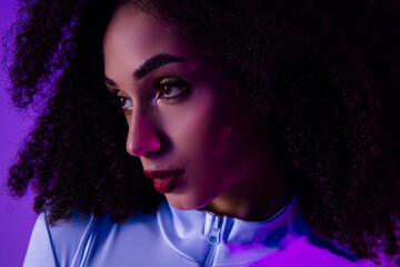 Stylish young woman with bold makeup in purple neon lighting, wearing a chic bodysuit, showcasing...