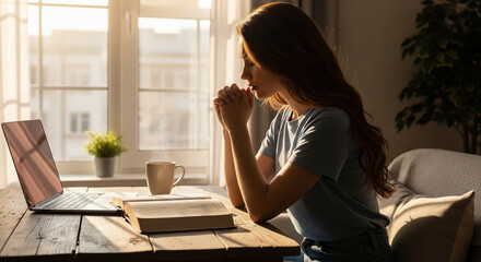 Young woman praying by a window with Bible and morning light