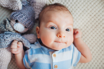 Close up of cute newborn baby lying on couch playing with knitted toy wearing bodysuit. Infant...