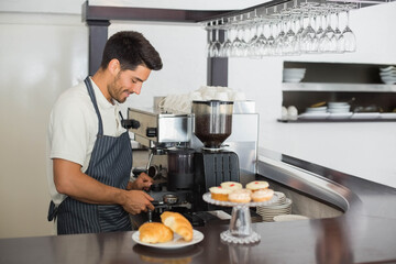 Male barista operating espresso machine behind counter with portafilter, croissants and cupcakes