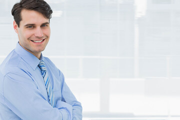Man wearing dress shirt and striped tie standing with crossed arms at office window, copy space