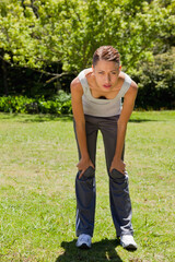 Woman pausing during outdoor workout on grassy field in public park wearing white running shoes