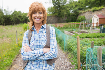Mature woman standing on gravel path by raised beds with netting wearing plaid shirt, tweed vest