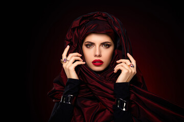 Elegant young woman in luxurious red scarf posing with a confident gaze against a gradient...