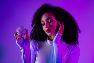 Glamorous young woman posing with beauty product under vibrant neon purple lighting