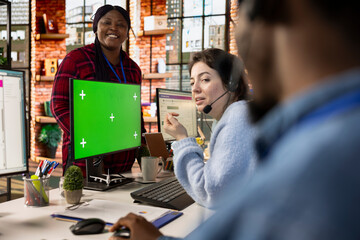 Call center agents laughing in office whit green screen mockup PC monitors, taking break. Customer support workspace colleagues having fun together at desks in front of chroma key computer display