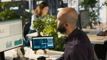Accountant in office inputting financial figures on PC, giving report files to coworkers. Arab man in workplace crosschecking data on computer, giving documents to colleagues, camera A