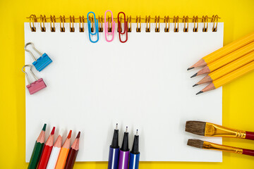 Flat lay of school and art supplies with blank notebook on yellow background with copy space.