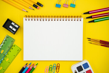 Flat lay of school and art supplies with blank notebook on yellow background with copy space.