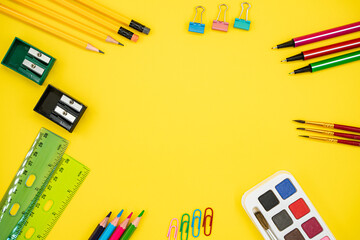 Flat lay of colorful school and art supplies on yellow background with copy space.