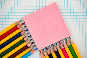 Colorful pencils with pink sticky note on graph paper. Back to school concept.