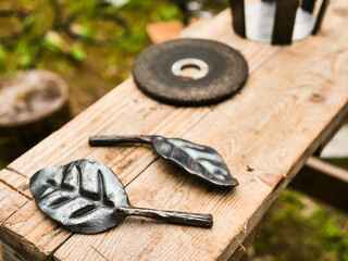 Making of a metal rose bouquet for a bride with flower allergy. Romantic gesture. Blacksmith and welder craft and skill. Selective focus. Leaf on a wooden table and tools out of focus.