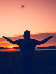 A person is standing in a field with a sunset in the background. The person is wearing a hoodie and...