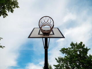 Basketball backboard mounted on a poll in a outdoor playground. Blue cloudy sky background. Popular international sport game.