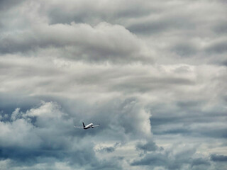 A plane is flying through a cloudy sky. The clouds are dark and heavy, giving the scene a moody and...