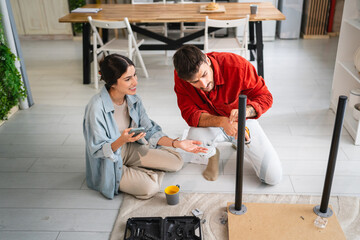 Couple assembling furniture while consulting instructions on smart phone