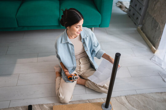 Woman assembling furniture at home reading instructions manual