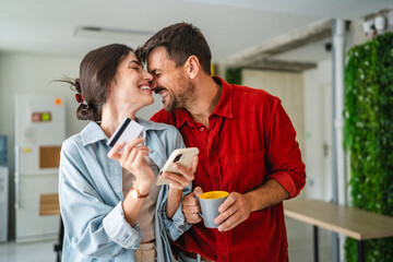 Happy couple making online shopping using smart phone and credit card at home