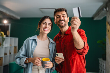 Happy couple making online payment using credit card and cellphone at home