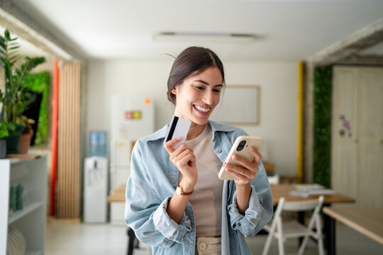Young woman holding credit card and smart phone smiling at home