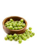 Fresh green gooseberries are displayed in a wooden bowl, with some berries scattered around, showcasing their vibrant color and natural texture in a clean, minimalistic setting