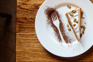 Dessert slice on a white plate with cocoa powder artfully arranged in the shape of a fork,...