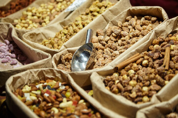 Assorted nuts and dried fruits displayed in paper bags with a metal scoop, showcasing a vibrant variety of textures and colors in a market setting, inviting culinary exploration