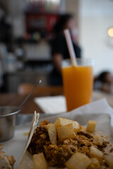 A breakfast taco with chorizo eggs and potato on flour tortilla. Orange juice and salsa in the background.